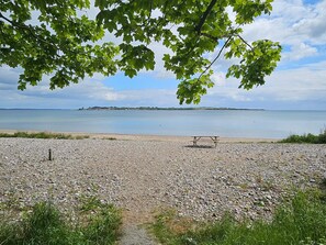 A pebbled beach with a picnic table and a distant island. - 4 Person Holiday Home in Aabenraa (Aabenraa)