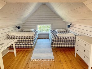 A small attic bedroom with two beds, a window, and a wooden floor.