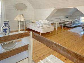 A loft-style bedroom with a wooden floor, a bed with white bedding, a checkered sofa, and a small table. - 4 Star Holiday Home in Ellos (Ellos)
