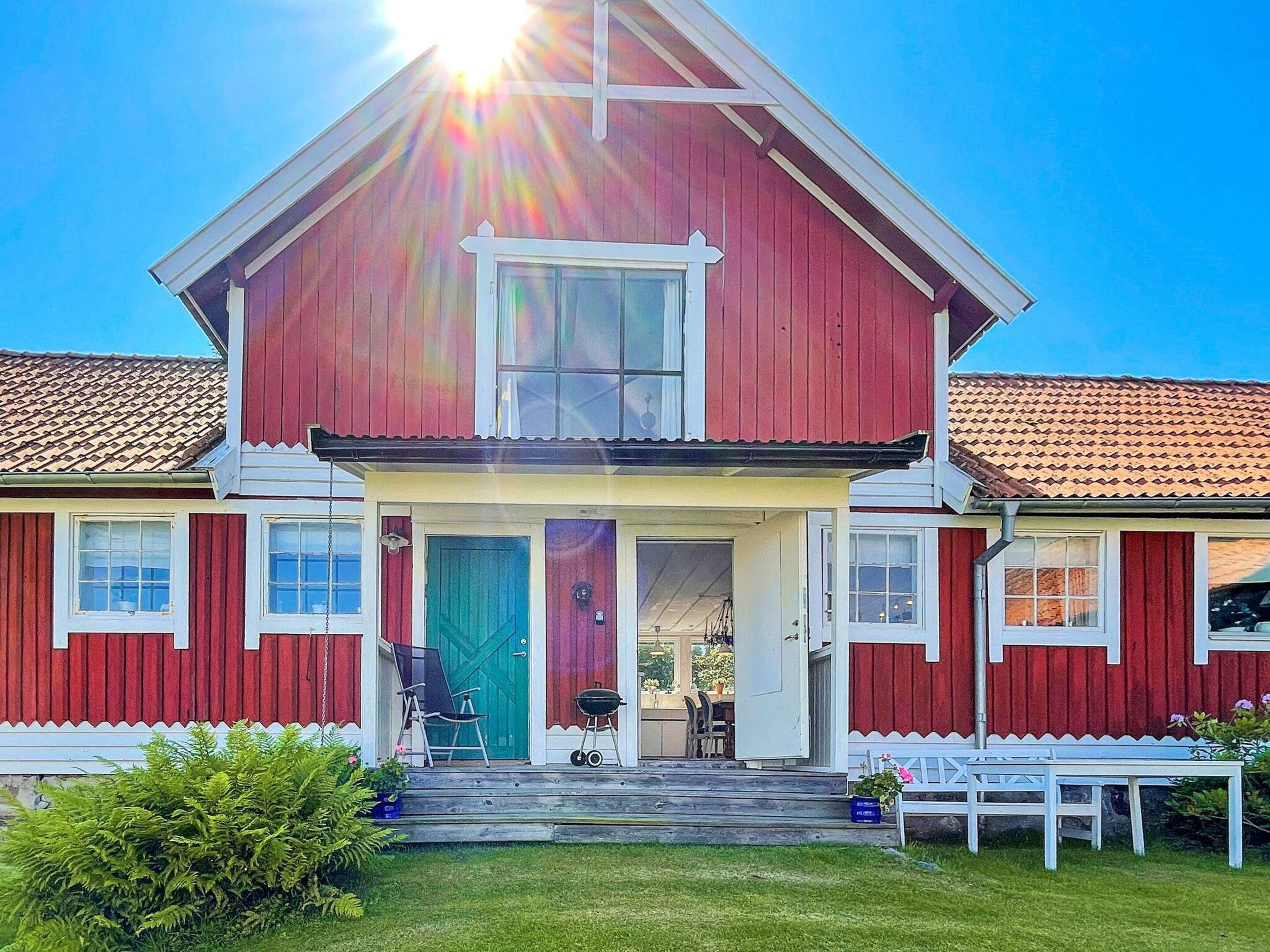 Ein zweistöckiges Haus mit roter Fassade, einer Veranda und einem sichtbaren Garten.