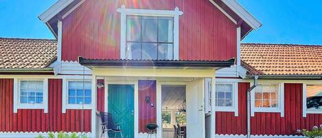 Ein zweistöckiges Haus mit roter Fassade, einer Veranda und einem sichtbaren Garten.