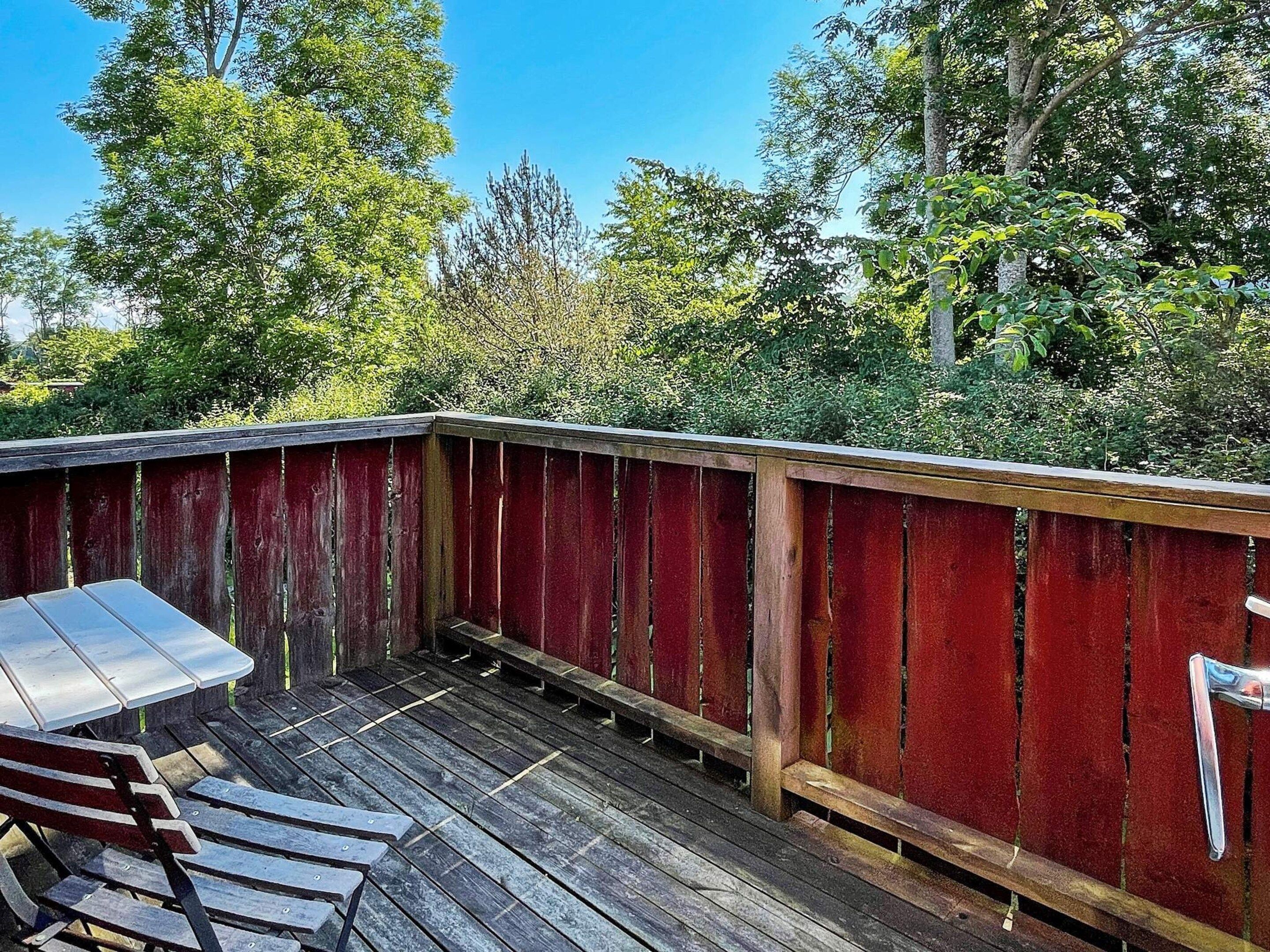A wooden deck with a metal table and benches, surrounded by trees.