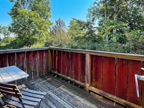 A wooden deck with a metal table and benches, surrounded by a red fence and trees. - 4 Star Holiday Home in Ellos (Ellos)