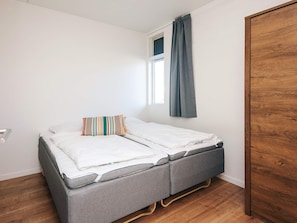 Une petite chambre avec un lit simple, une armoire en bois, une fenêtre avec des rideaux et un plancher en bois.