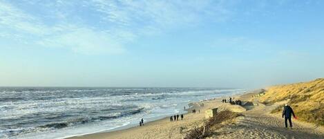 A sandy beach with people walking along the shore and a person carrying a red object.