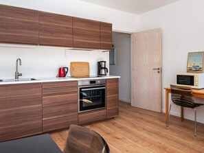 Eine moderne Küche mit Holzschränken, einer Edelstahl-Spüle, einem roten Wasserkocher, einer Kaffeemaschine und einer Mikrowelle auf einem Holztisch.