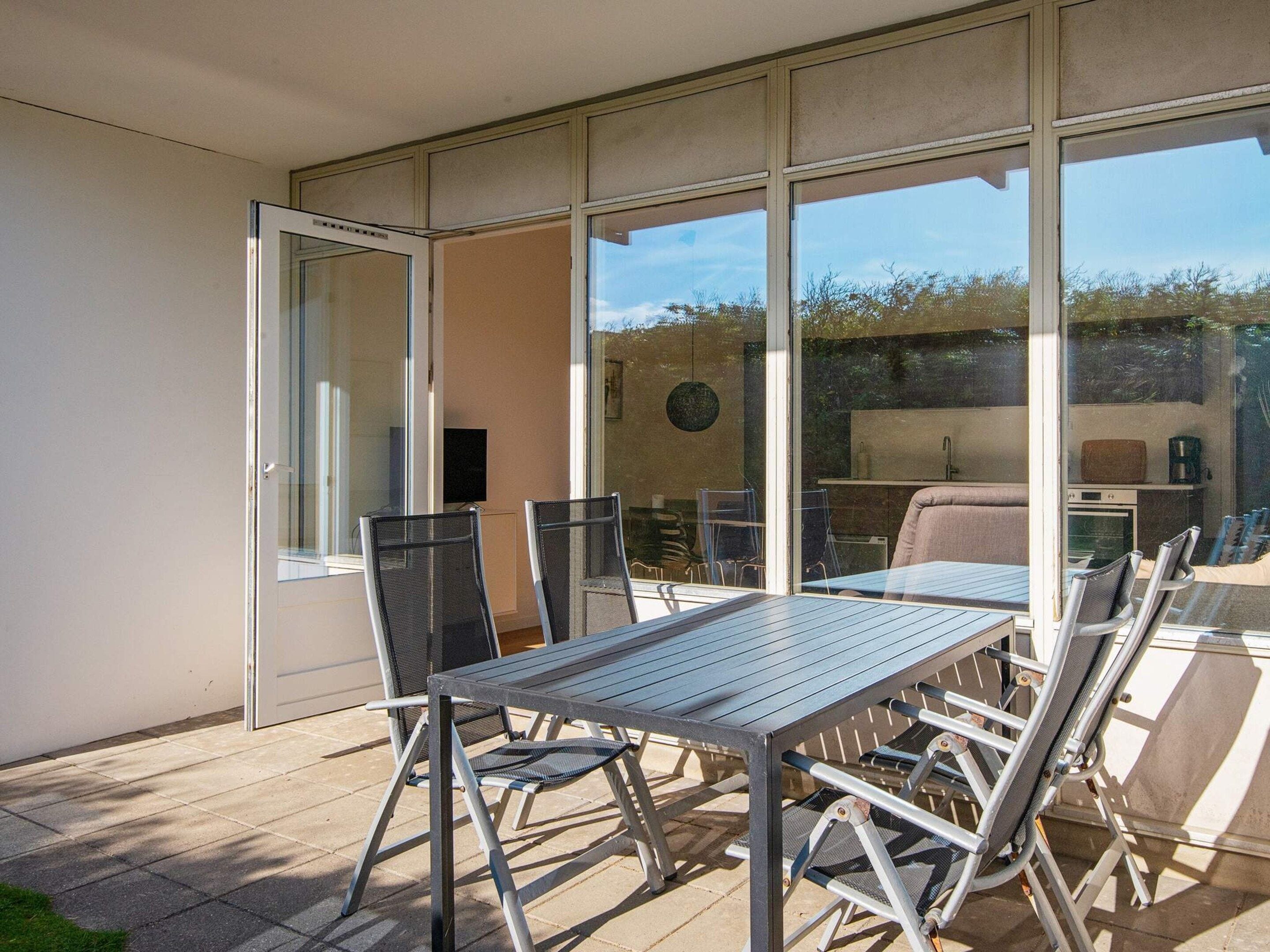 A patio with a table and chairs, a sliding glass door, and a view of a kitchen area.