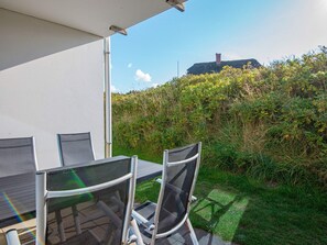 An outdoor patio with a table and chairs, surrounded by greenery and a view of a hill. - 4 Star Holiday Home in Ringkobing (Ringkobing)