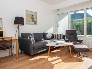 Una sala de estar moderna con un sofá gris, una mesita de centro, un sillón gris y un ventanal con vistas a la vegetación y montañas.