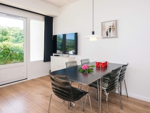 Ein stilvolles Esszimmer mit einem großen Tisch, Stühlen, einem Fernseher und Blick auf Grünflächen.
