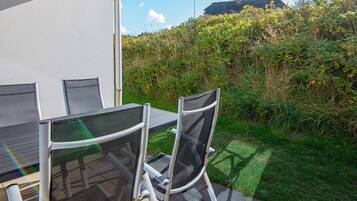 An outdoor patio with a table and chairs, surrounded by greenery and a view of a hill.