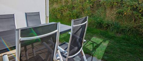 An outdoor patio with a table and chairs, surrounded by greenery and a view of a hill.