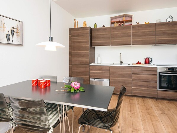 Una cocina moderna con armarios de madera, un lavamanos de acero inoxidable y una zona de comedor con mesa y sillas.