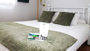 En pænt redt seng med et grønt strikket tæppe og to puder, et hvidt sengegavl og en sengebordlampe.
