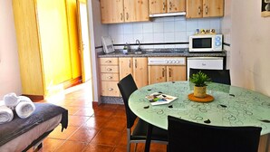 Et kompakt køkken med træskabe, en mikrobølgeovn, komfur og et spisebord med stole.