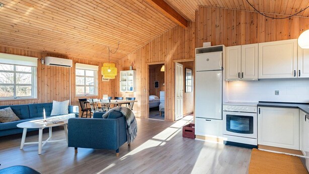 A spacious living area with a wooden ceiling, a dining table, and a kitchen with white cabinets and appliances. - 5 Person Holiday Home in Hals (Hals)