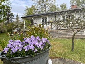 A metal planter with purple flowers in front of a house with a wooden deck and a metal fence. - 4 Person Holiday Home in Ronneby (Ronneby)