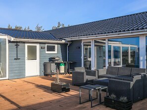 A covered patio with outdoor furniture, a grill, and a sliding glass door leading to a deck.