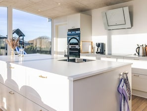 A modern kitchen with a large island, stainless steel appliances, and a view of a house through the window. - 5 Star Holiday Home in Lokken (Lokken)