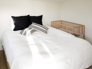 A bedroom with a bed, pillows, and a wooden crib.
