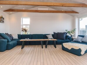 A modern living room with a wooden floor, a dark blue sofa set, a wooden coffee table, and a large window providing natural light.