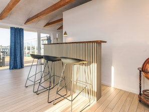 A modern interior with a wooden ceiling, a bar area with stools, and a view through a large window.