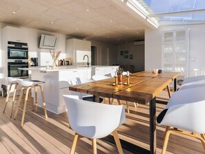 Une cuisine moderne avec des meubles blancs, une table à manger en bois et des chaises blanches.