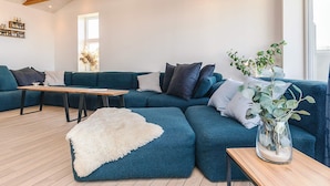 A modern living room with a sectional sofa, a wooden coffee table, and a white furry rug. - 5 Star Holiday Home in Lokken (Lokken)