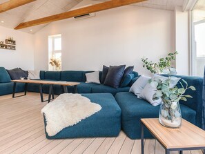 A modern living room with a sectional sofa, a wooden coffee table, and a white furry rug. - 5 Star Holiday Home in Lokken (Lokken)