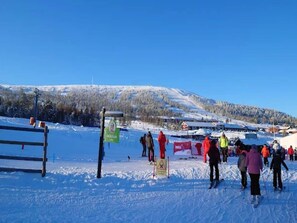 En snötäckt skidbacke med skidåkare, ett trästaket och en vägskylt.