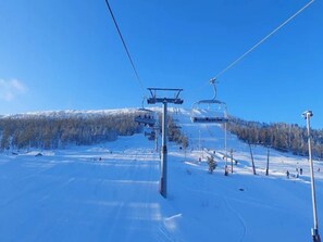 En skidlift med vajrar och stolar, ett snötäckt landskap och en klarblå himmel.
