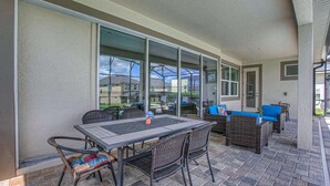 An outdoor patio with a table and chairs, a covered area with a glass door, and a view of neighboring houses. - Amazing 5 Star Villa on Solara Resort With Private Pool, Orlando Villa 6119 (Kissimmee)
