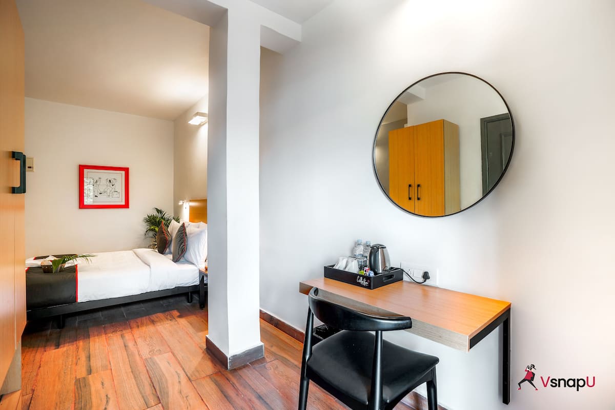 Una habitación de hotel moderna con una cama, un escritorio, una silla, un espejo redondo y un cuadro en la pared.