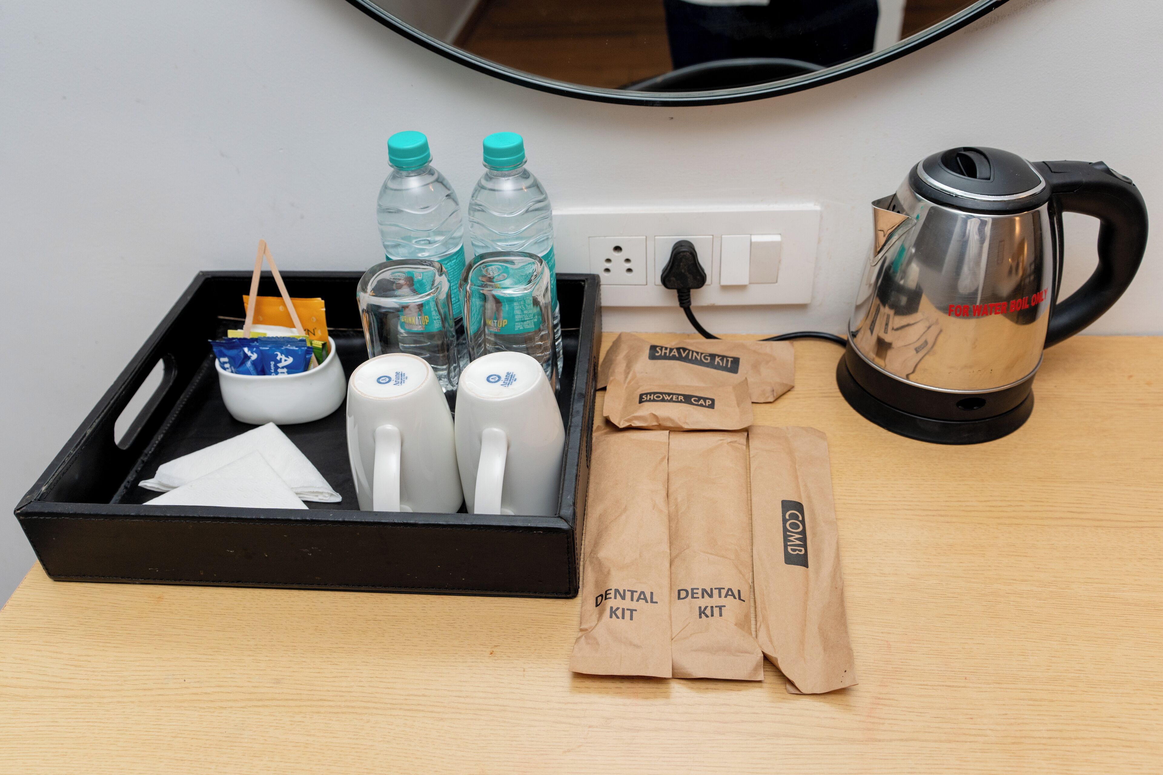 Un plateau contenant un kit de rasage, une trousse de soins dentaires, des bouteilles et une bouilloire, posé sur une table en bois.