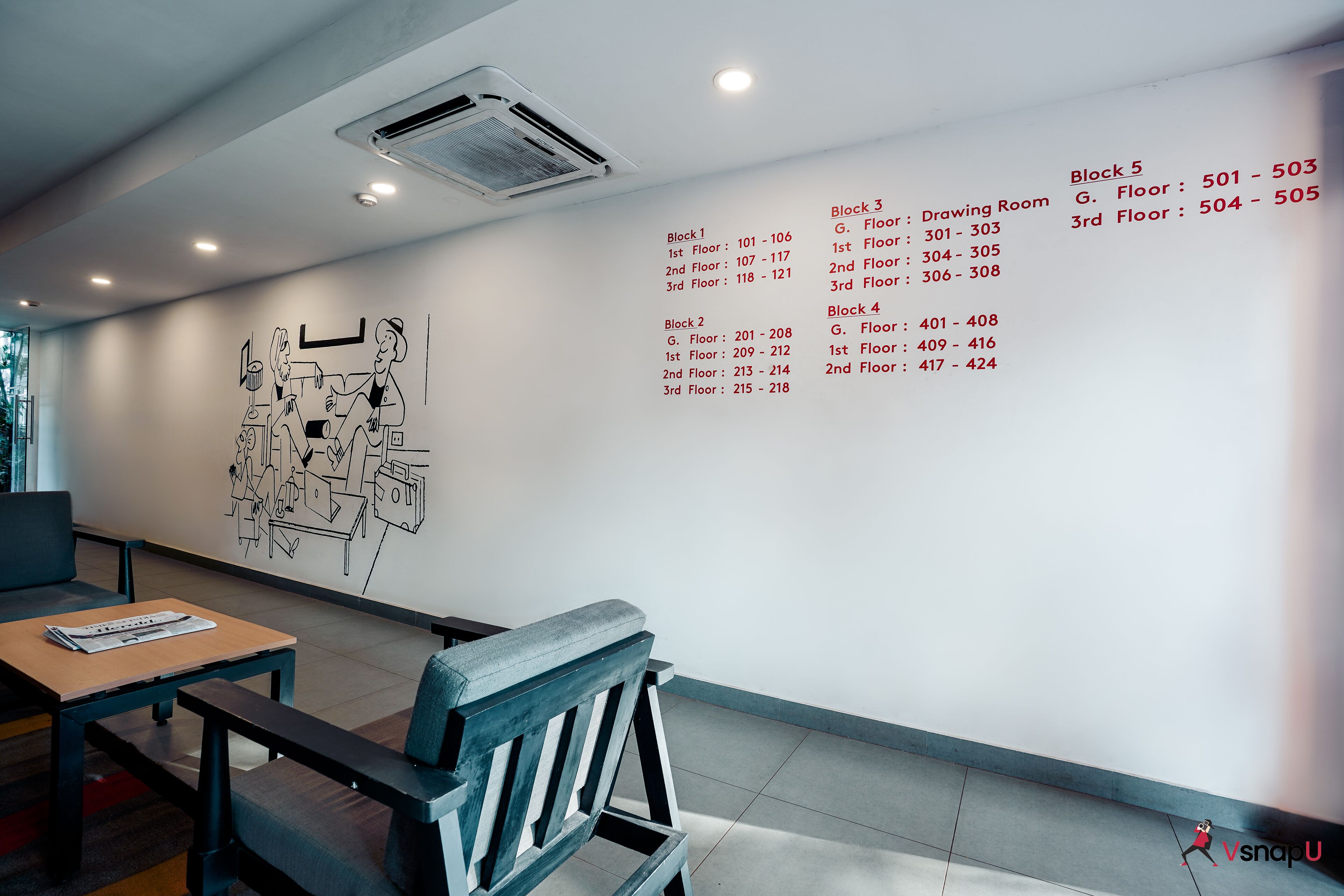 A modern interior with a wall-mounted artwork, seating area, and a list of room numbers and floors.