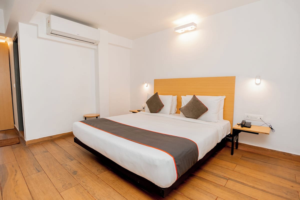 Habitación de hotel ordenada con una cama grande, una mesita de noche con teléfono y un aire acondicionado instalado en la pared.