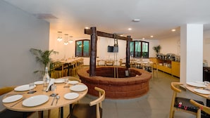 A restaurant with round tables, a central brick structure, and wooden chairs. - Magnum Resorts Candolim (Candolim)