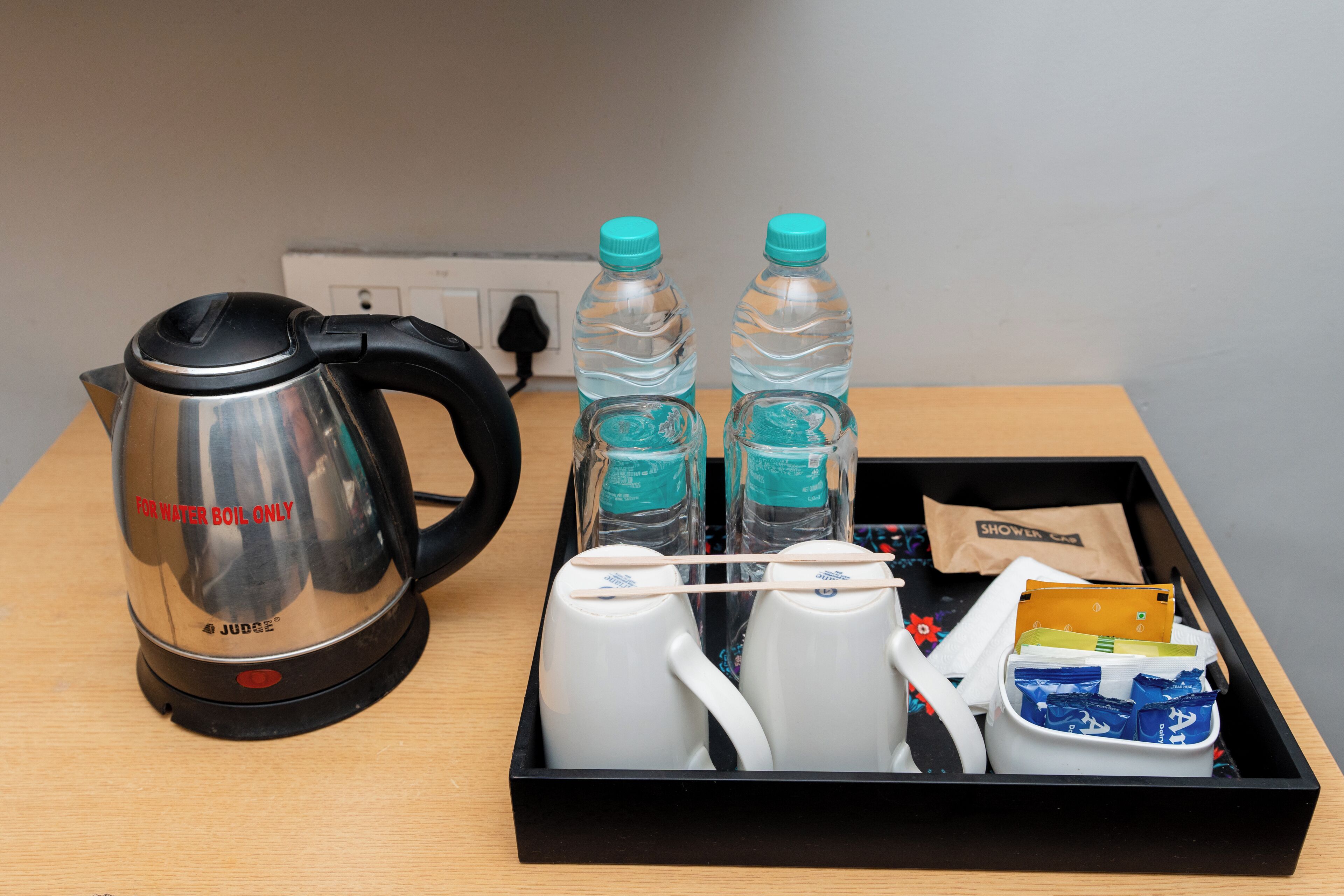 Ein Tablett mit einem Wasserkocher, zwei Wasserflaschen, einer weißen Tasse und einer kleinen Packung.