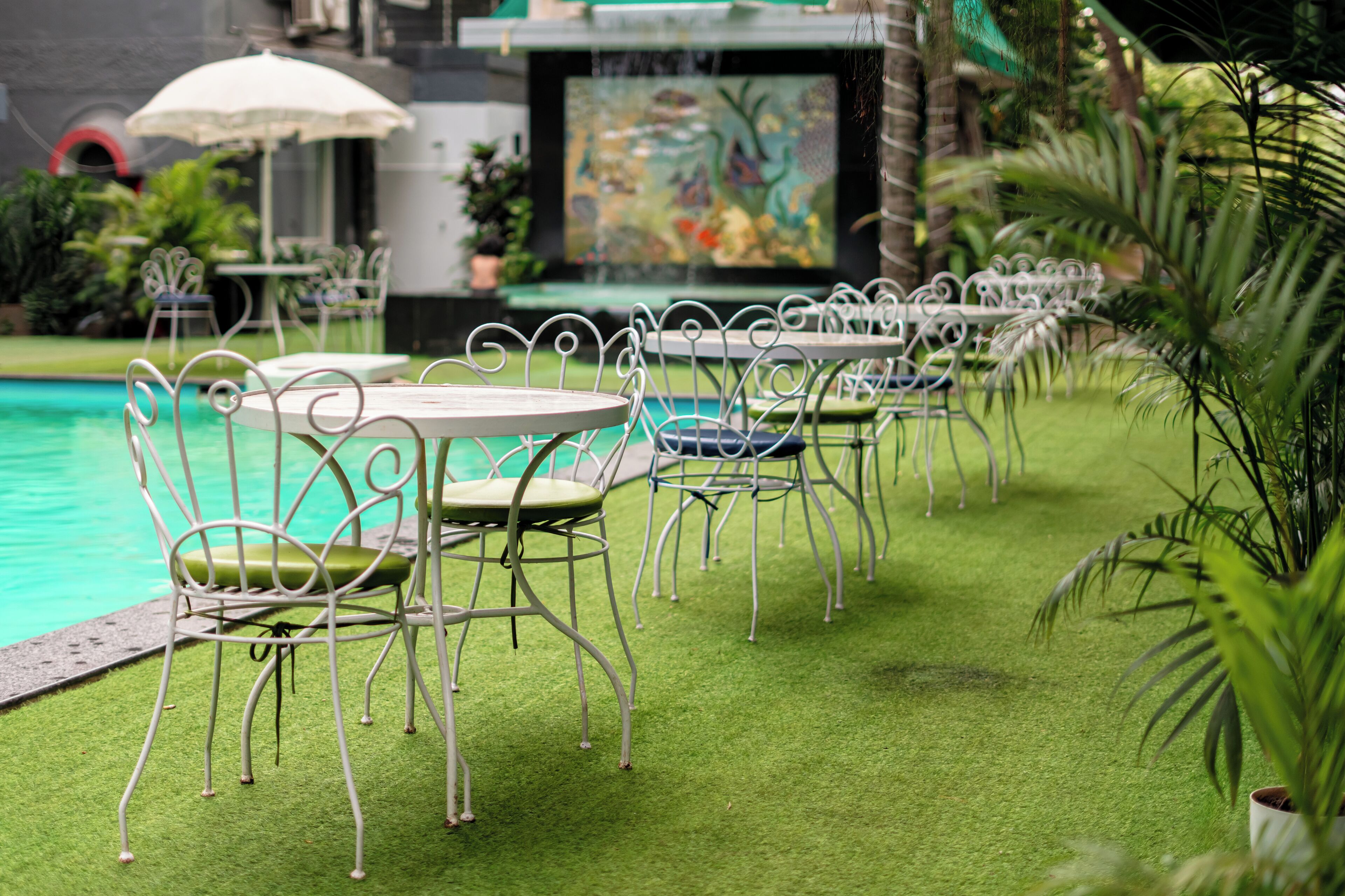 Outdoor seating with tables and chairs, a pool, and a mural in the background.