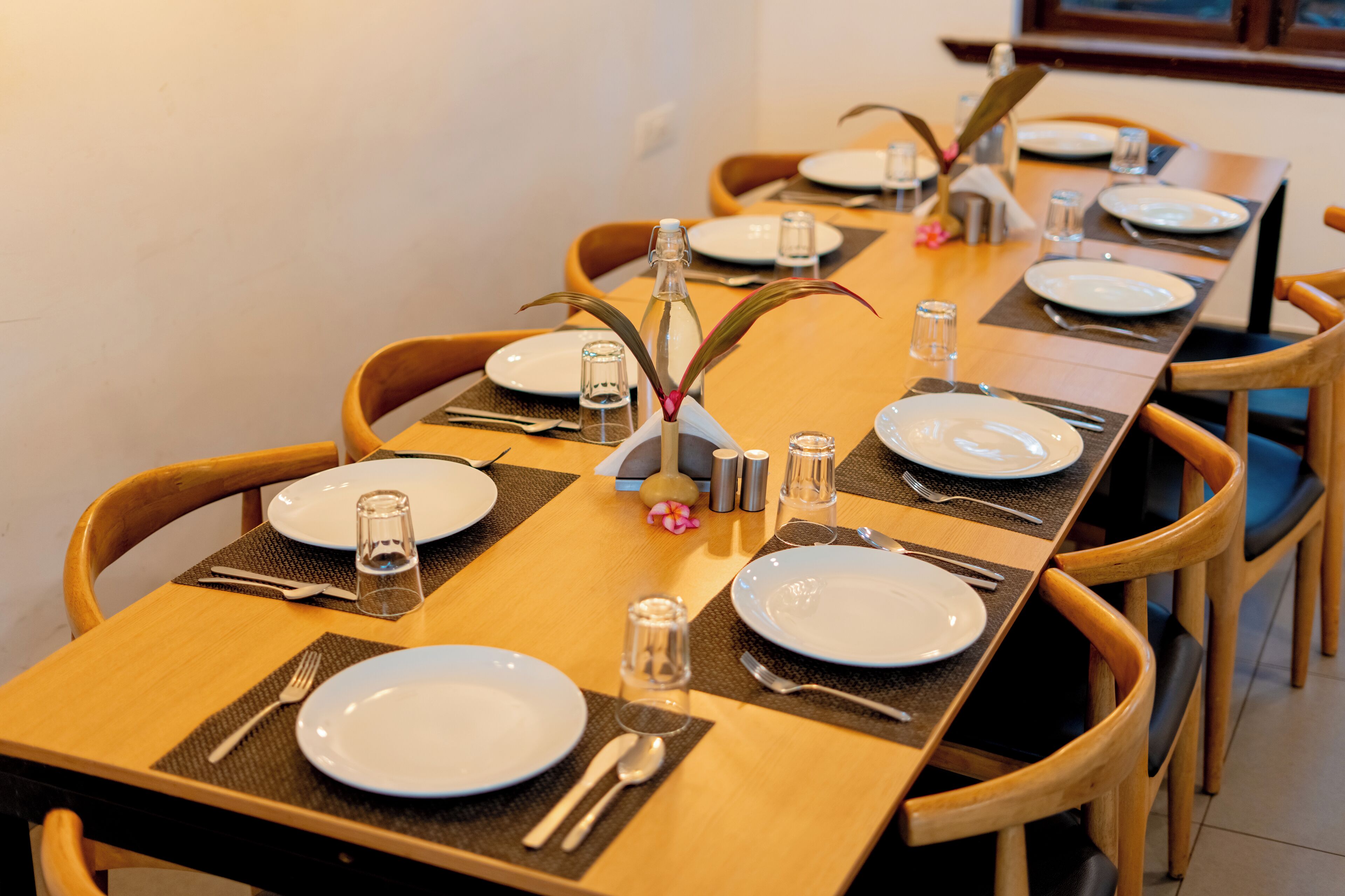 A dining table set with plates, cutlery, and glasses, surrounded by wooden chairs.