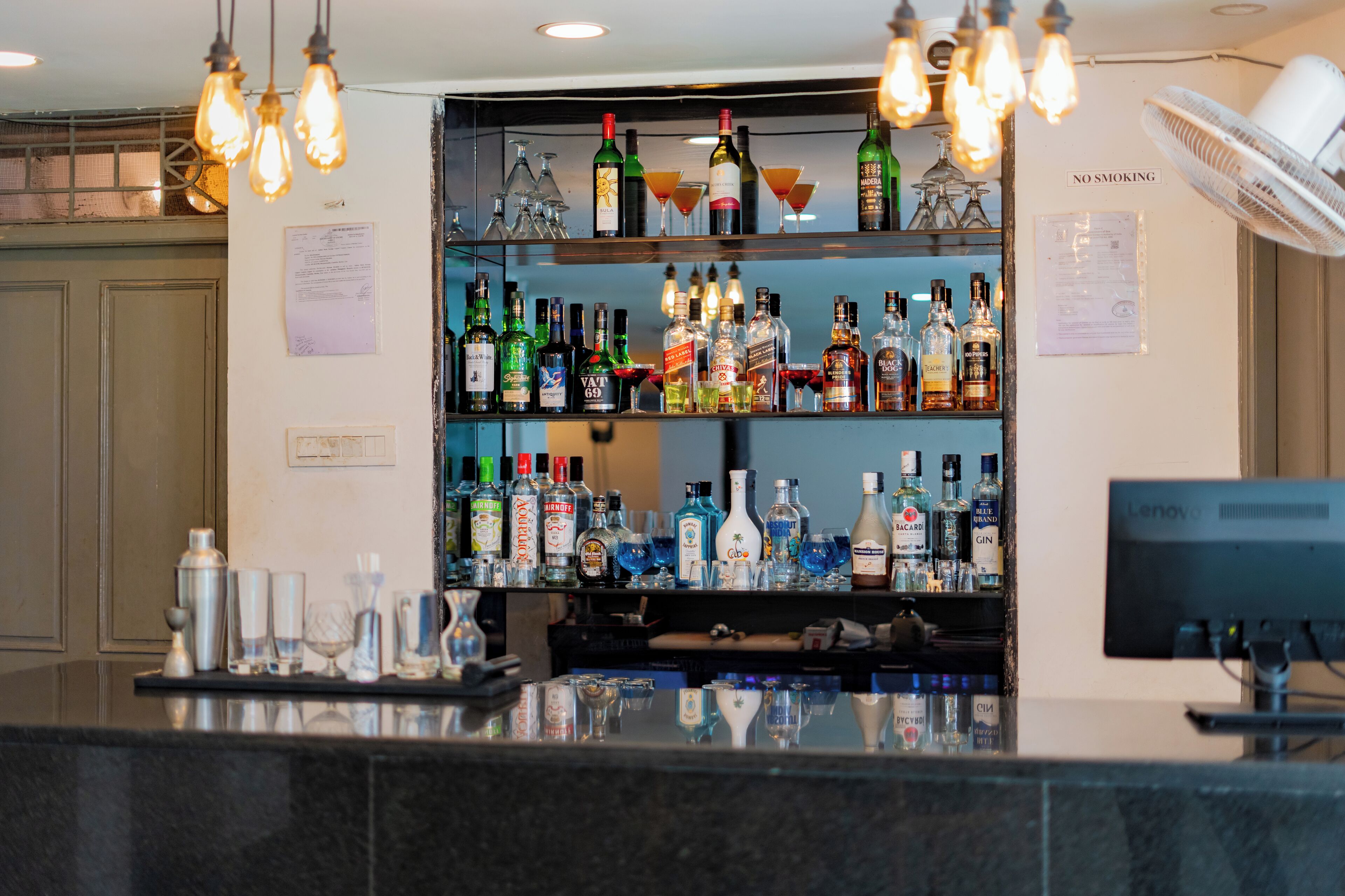 A bar area with shelves of liquor bottles, a computer monitor, and a 'No Smoking' sign.