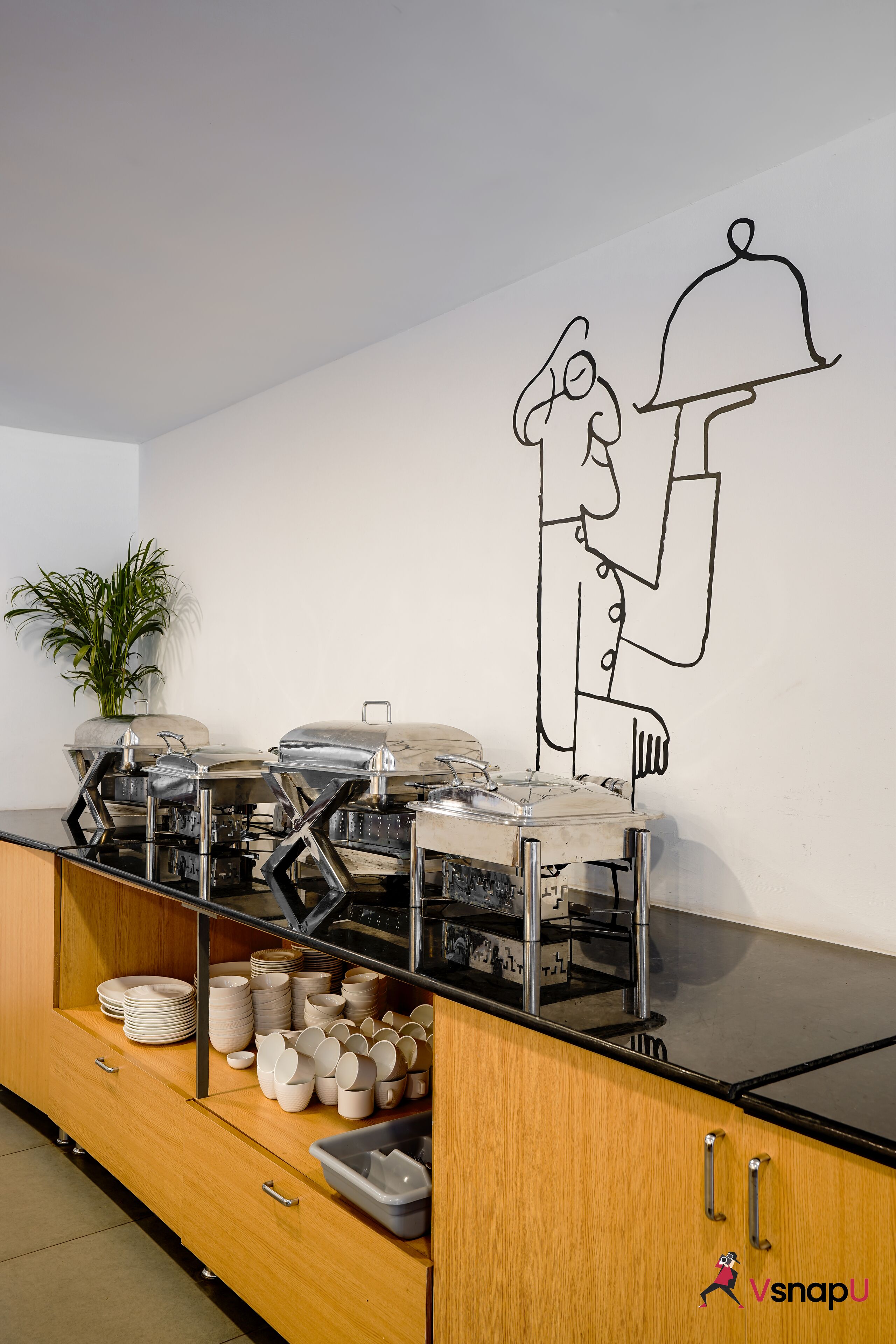 A kitchen with a buffet setup, a potted plant, and a wall mural.