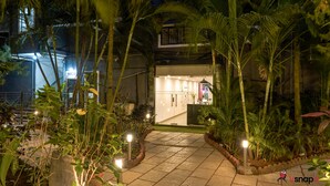 A well-lit pathway leading to a building with a modern design, surrounded by lush tropical plants. - Magnum Resorts Candolim (Candolim)