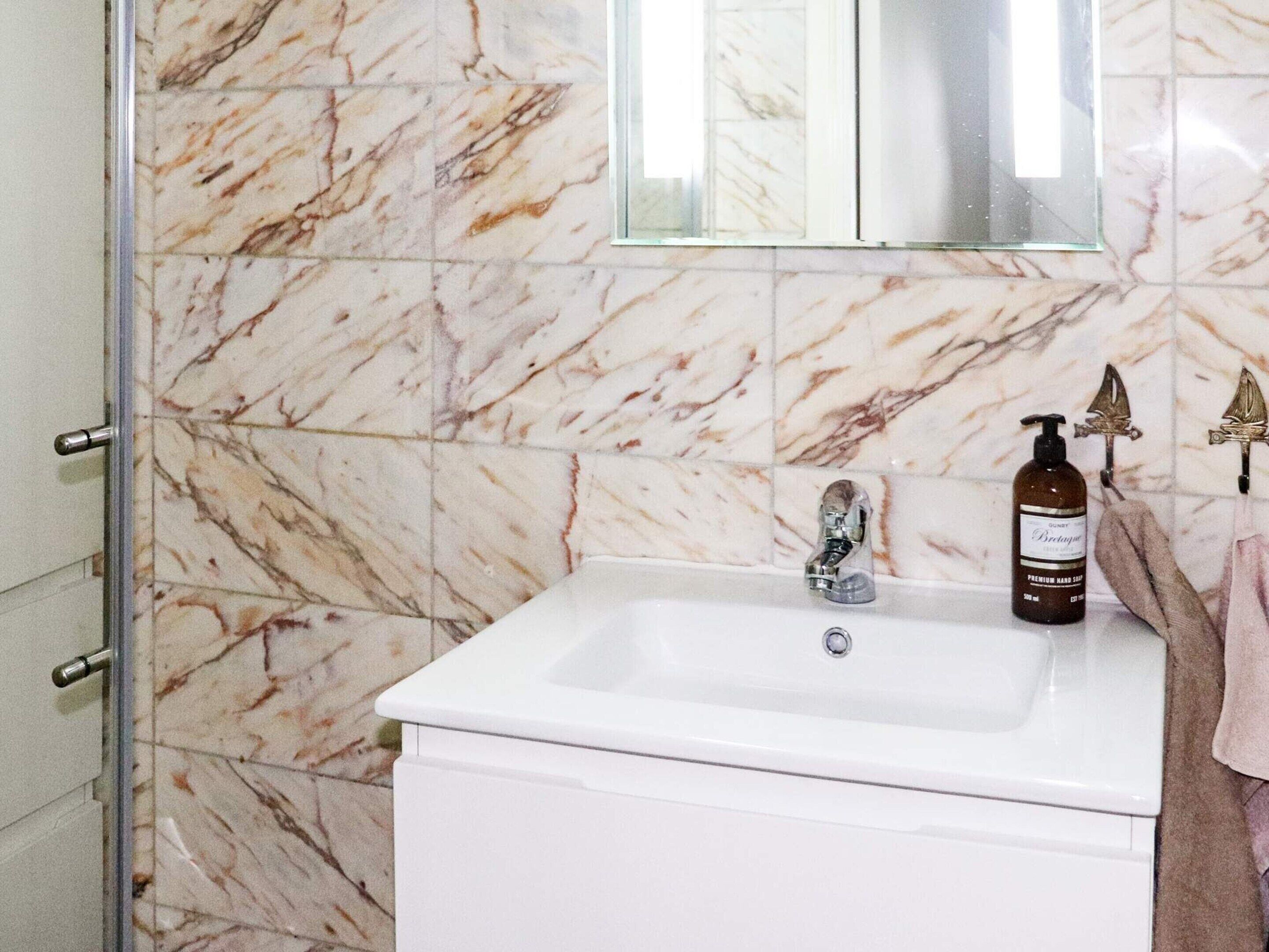 Un baño con lavamanos blanco, paredes de mármol y cabina de ducha de vidrio.