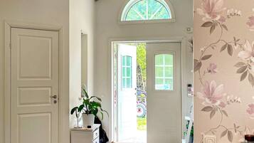 A hallway with a white door, a potted plant, a small cabinet, and a patterned rug.