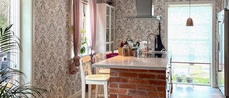 A kitchen with a brick island, wooden chairs, a hanging light, and a window with curtains.