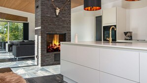 A modern kitchen with a built-in fireplace, white cabinetry, and a wooden ceiling. - 8 Person Holiday Home in Knebel (Knebel)
