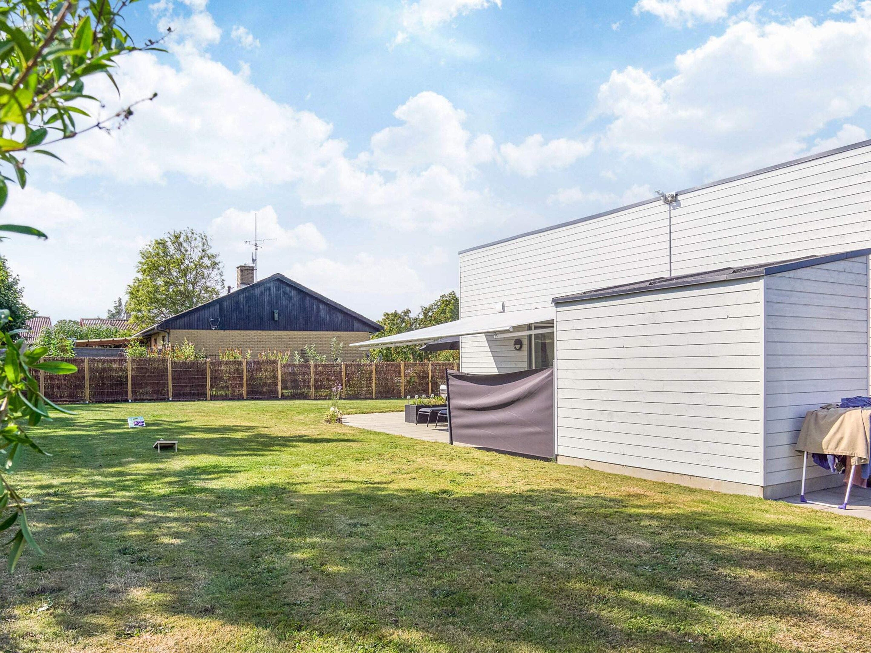 Un patio trasero residencial con área cercada, un porche techado y una casa con techo oscuro.