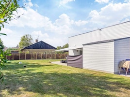 A residential backyard with a fenced area, a covered patio, and a house with a dark roof.