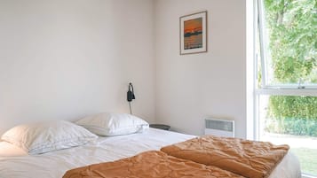 Un dormitorio con cama, ventana, calefactor en la pared y un cuadro.